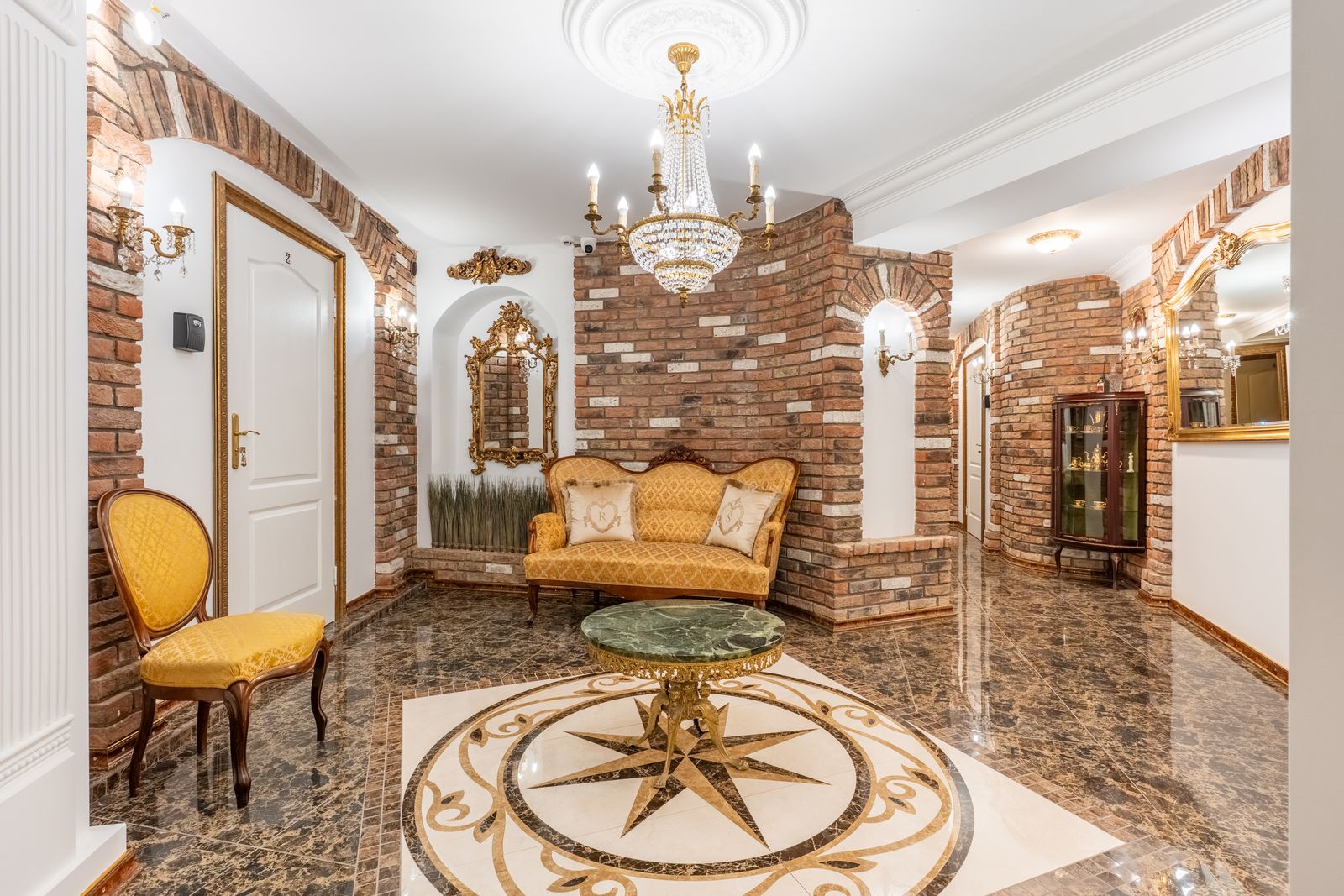 Entrance hall with an antique sofa, a gilded mirror and a crystal chandelier under brick arches — Underground Kingdom, Kaunas